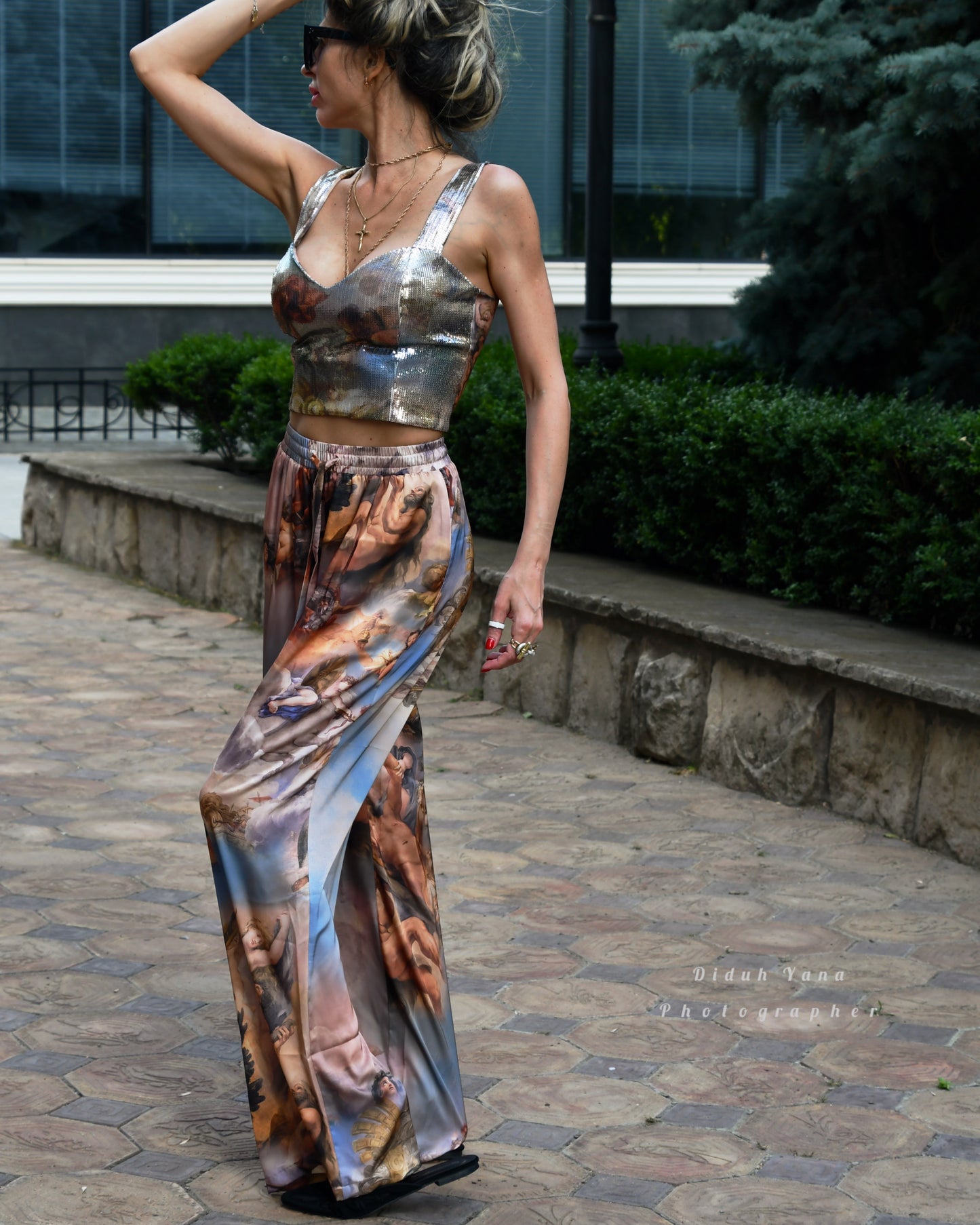 A person wearing a sleeveless, maxi-length dress with a floral and angel graphic design, standing on a cobblestone pathway.