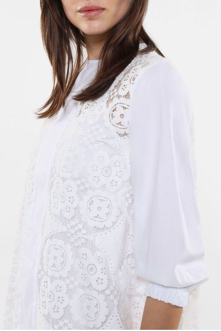 This image features a stylish white dress known as "Dress Twiggy," modeled by a woman wearing sunglasses. The dress showcases intricate lace detailing and a flowing silhouette, emphasizing elegance and contemporary fashion.