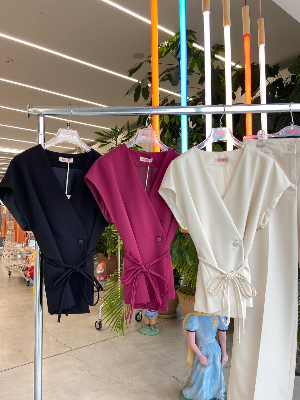 Three kimono vests hanging on a rack, available in black, pink, and white colors.