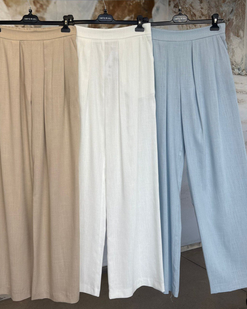 Three pairs of wide-leg pants in beige, white, and light blue hanging on a rack.