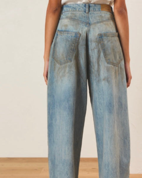Back view of blue jeans worn by a person on a wooden floor.