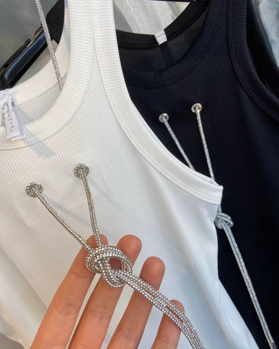 A close-up of a white top with a silver chain detail, displayed next to a black top with the same detail.