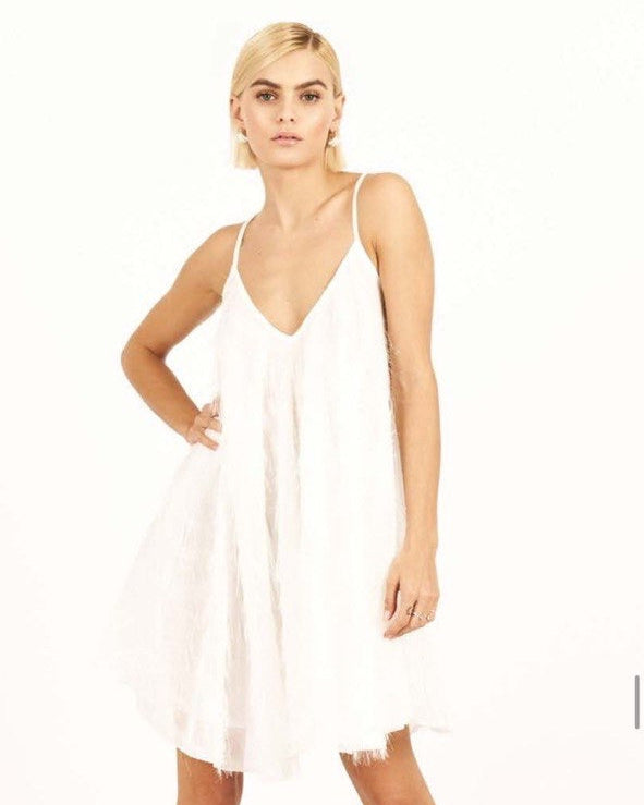 A female model standing, wearing a white sleeveless mini dress with a v-neckline.