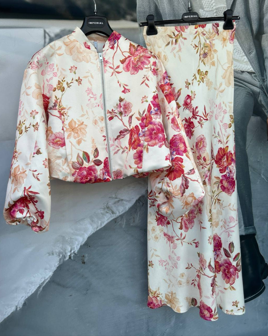 A floral printed two-piece outfit with a bomber jacket and matching skirt displayed on hangers.