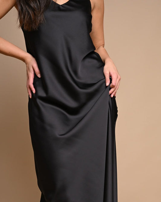A person wearing a black slip dress with a V-neck neckline and sleeveless top.