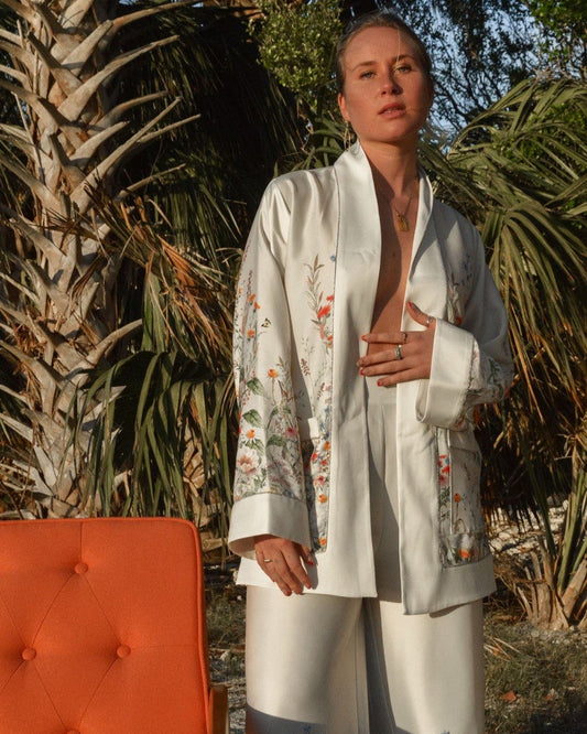A person wearing a white kimono with floral patterns, standing near a palm tree.