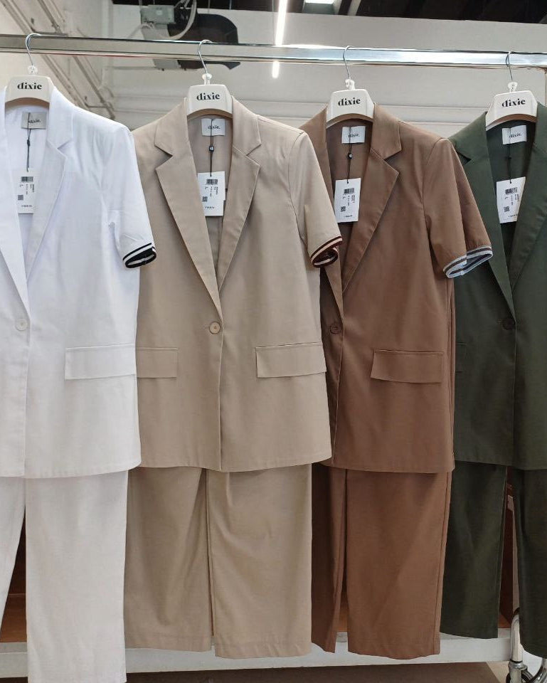 A selection of pant suits in beige, brown, green, and white, displayed on hangers.