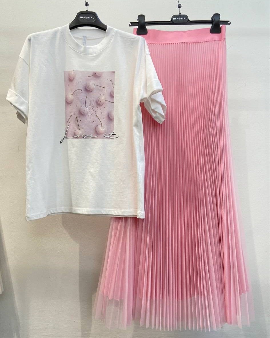 A white T-shirt with a cherry design on the front displayed on a hanger, alongside a pink pleated skirt, also on a hanger, against a white background.