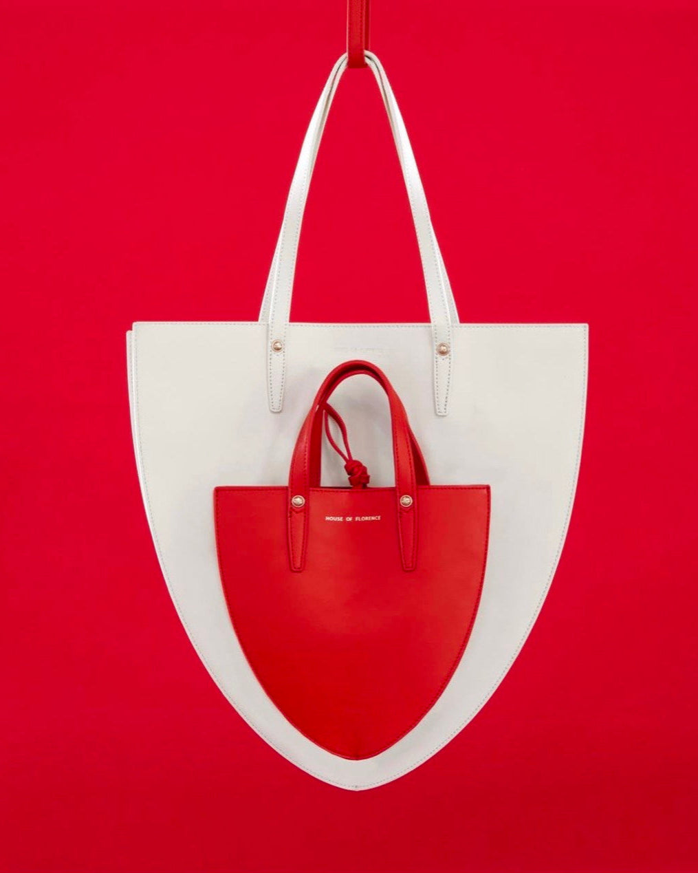 A white handbag with red detailing, displayed against a red background.