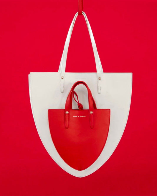 A white handbag with red detailing, displayed against a red background.