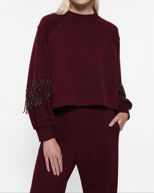 A woman wearing a maroon sweatshirt with fringe detailing on the sleeves, paired with matching maroon pants.