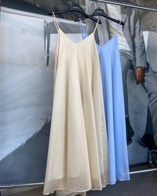 Beige and light blue dresses hanging on a rack with a blurred background.