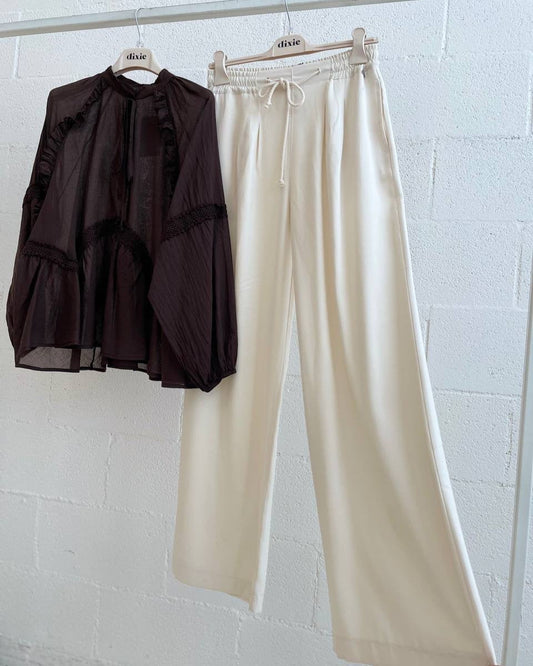 Black blouse and beige pants hanging against a white wall.