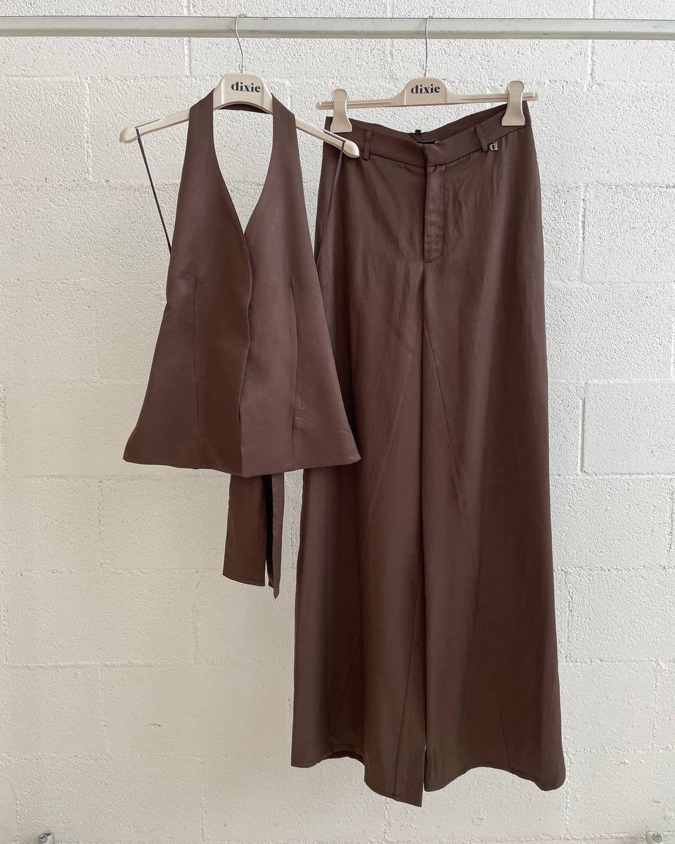 Brown vest and pants on hangers against a white brick wall.
