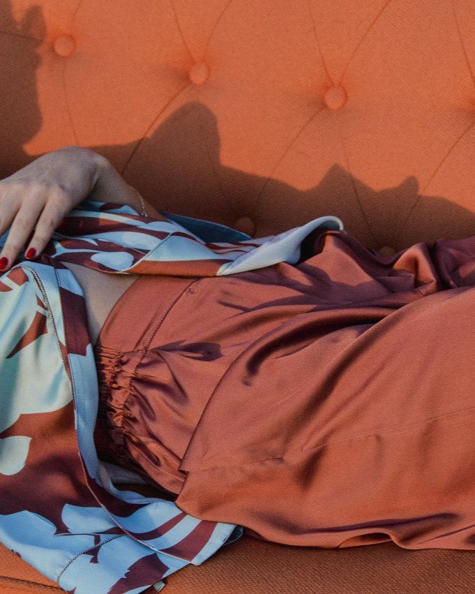 A person lying on an orange sofa covered with a multicolored floral patterned sheet.