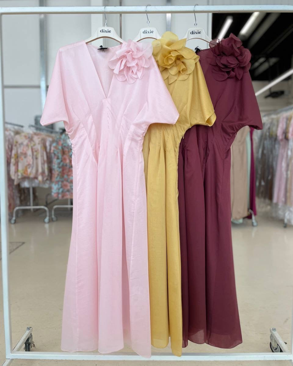 Three dresses hanging on display, from left to right: pink with a floral pattern, yellow solid color, and maroon with a floral pattern.