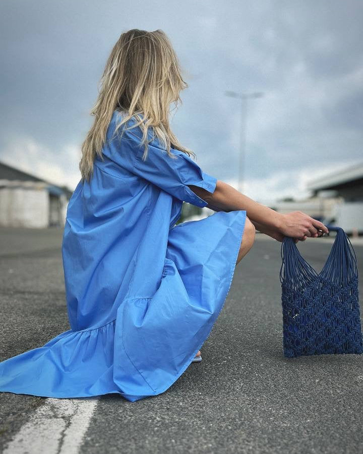 Person in a blue dress sitting on a street holding a blue bag.
