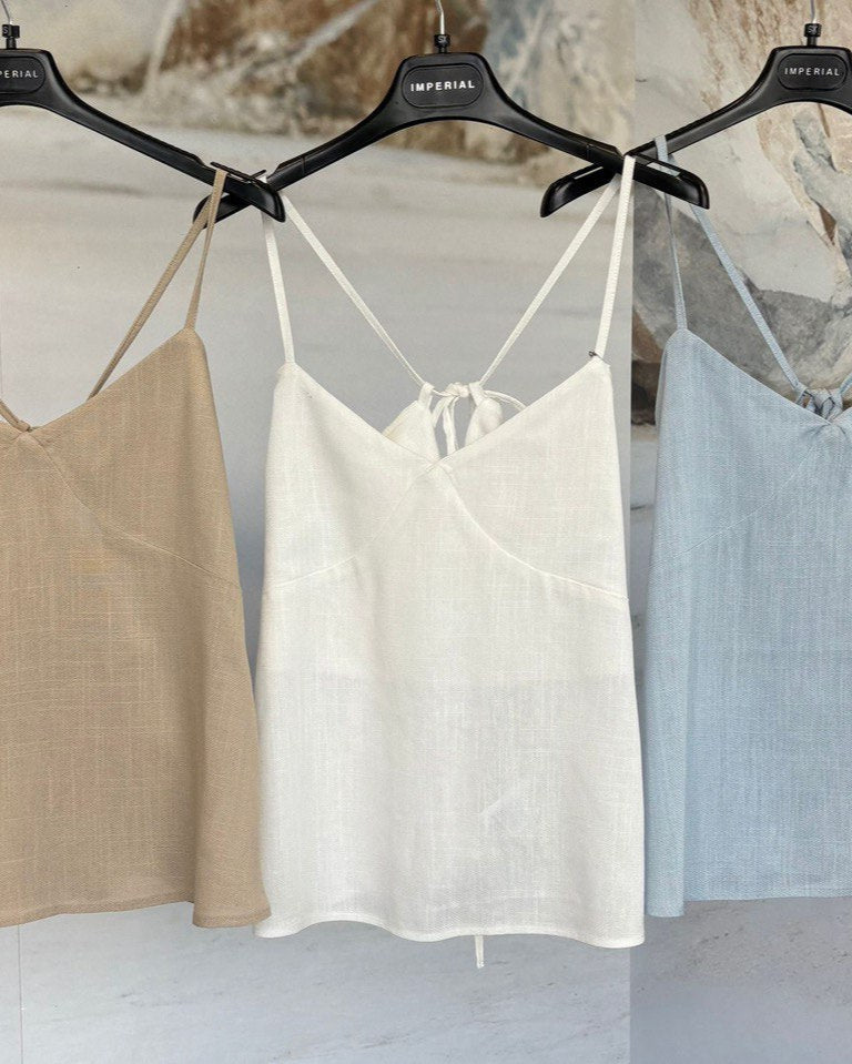 Three camisoles in beige, white, and light blue hanging on black hangers against a textured wall.