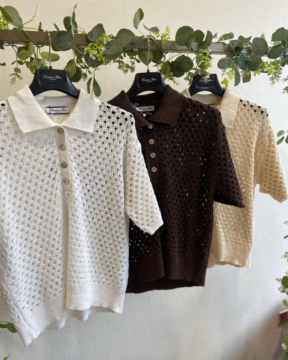 Three crocheted shirts in white, brown, and beige hanging with greenery in the background.