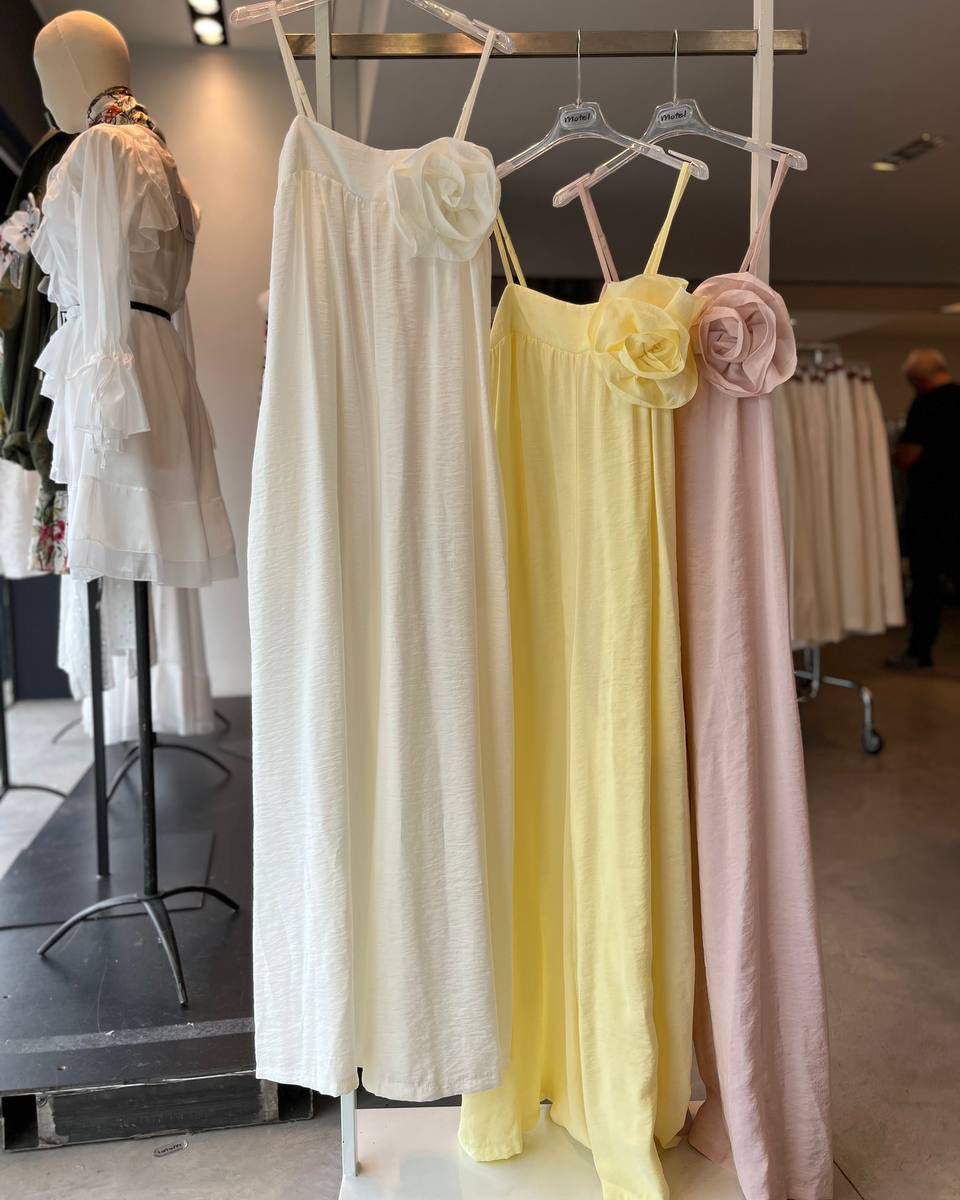 Three dresses in white, yellow, and pink hanging on a rack in a store setting.