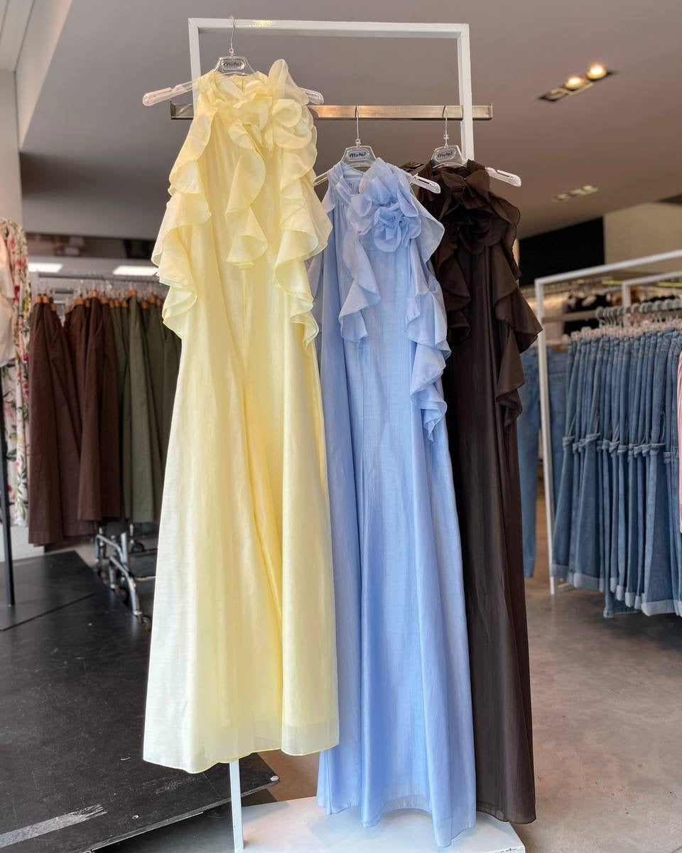 Three dresses in yellow, blue, and brown hanging on a rack in a store.