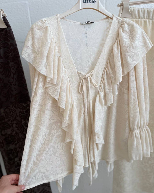 White lace blouse on a hanger against a white brick wall.