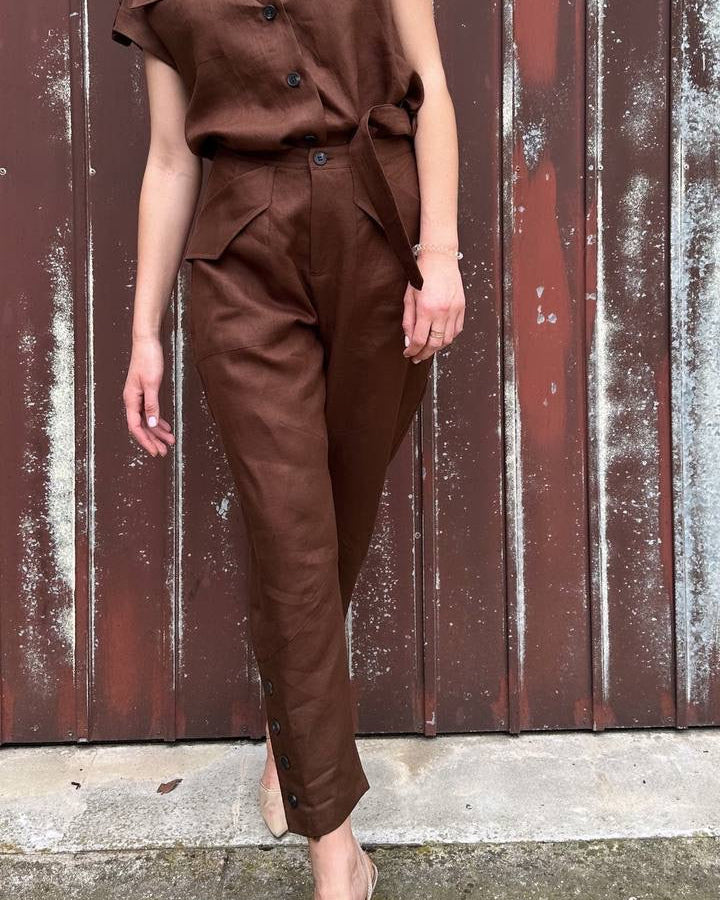 Woman wearing a brown outfit standing against a textured wall.