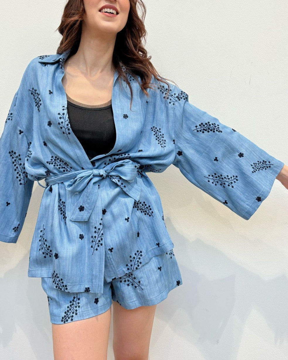 A woman wearing a blue floral cotton suit with a tie waist belt and long sleeves.
