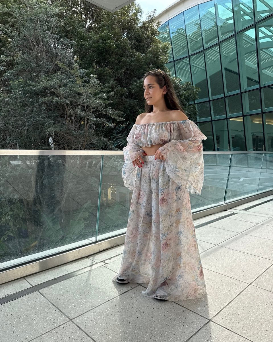 A woman standing on a balcony wearing an off-shoulder, floral chiffon maxi dress.