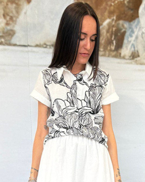 Woman wearing a white blouse with black floral patterns against a neutral background
