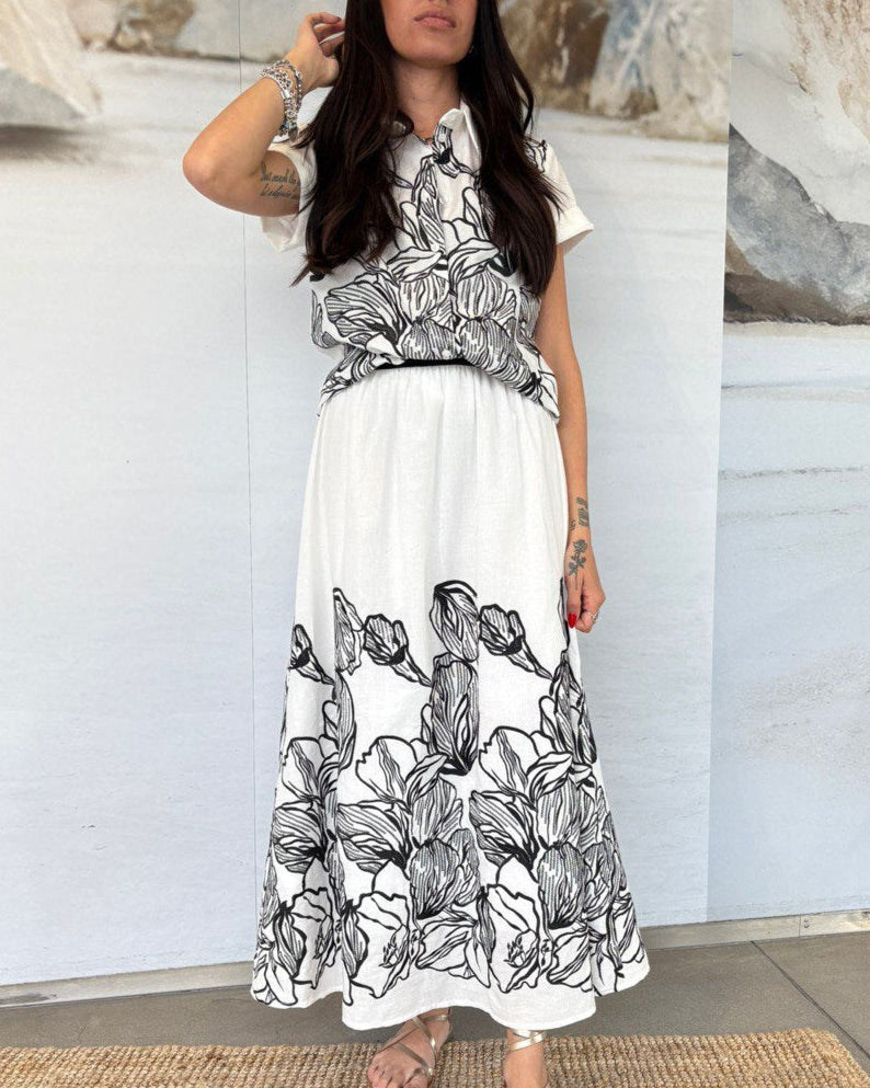Woman wearing a white dress with black floral patterns in an indoor setting.