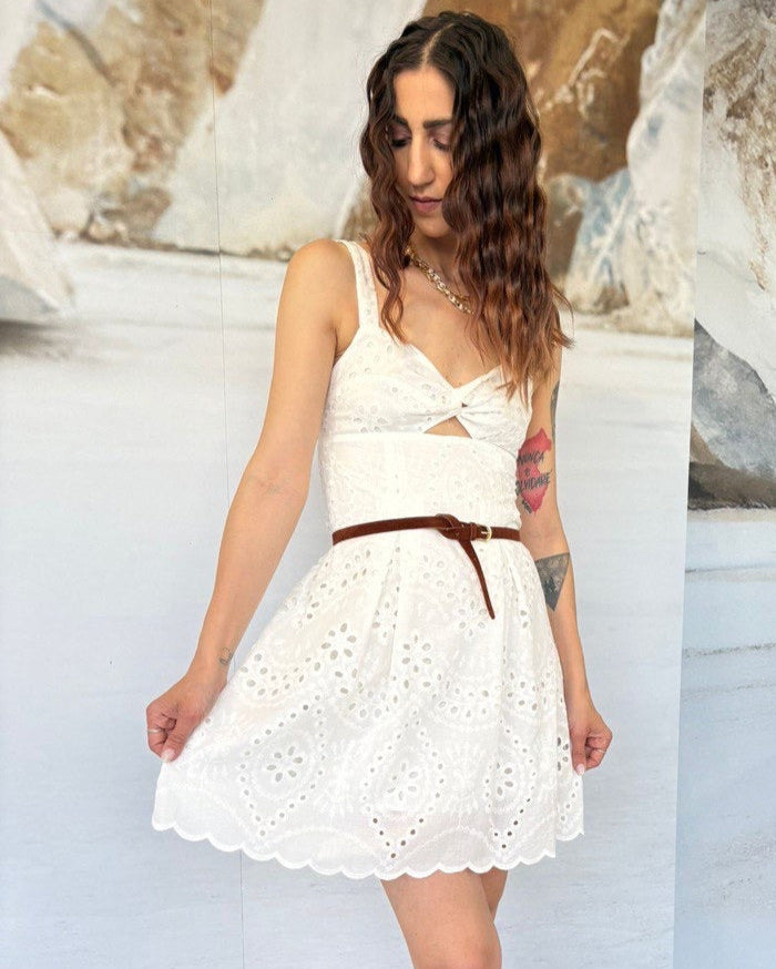 Woman wearing a white dress with a brown belt in front of a textured wall.