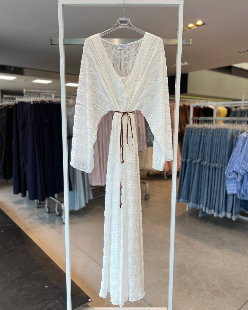 A white lace dress hanging on a hanger in a retail setting, with clothing items in the background.