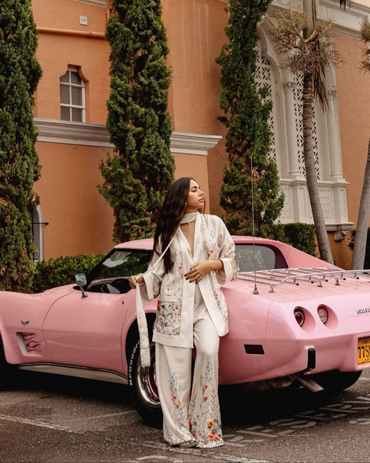 A person standing next to a pink car, wearing a white suit with a pattern.