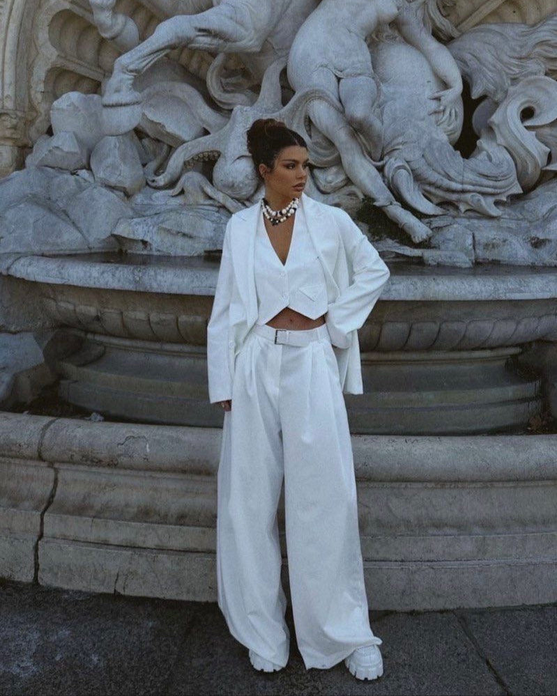 A person wearing a wide pants with belt, standing in front of a sculptural fountain.
